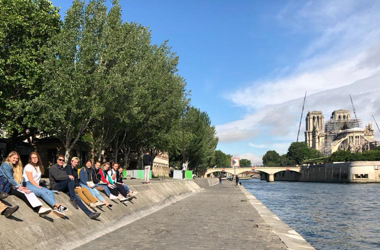 Students sit along the Seine River with Notre Dame in the background