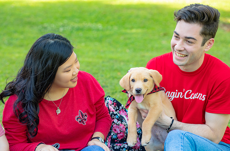 students in red UL gear playing with a puppy in a red bandana